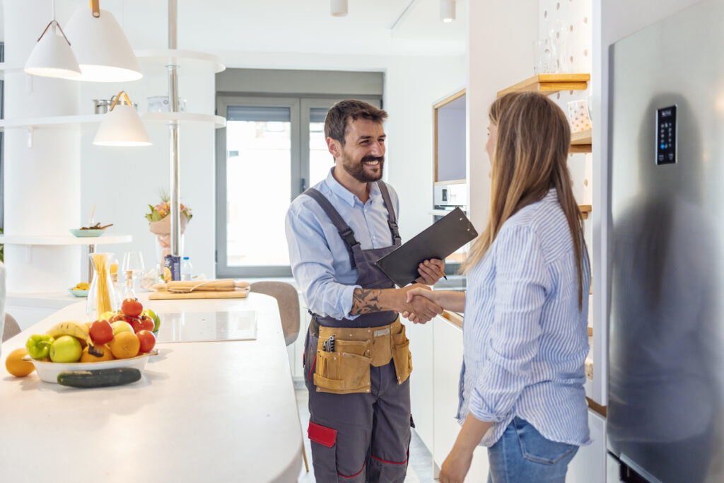 Young woman shaking hands with a male plumber in the kitchen